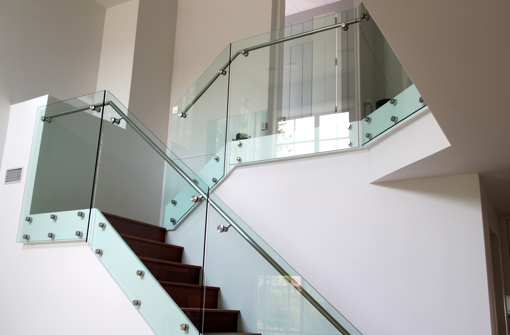 Garde-corps en verre avec fixations ponctuelles apparentes installé le long d'un escalier moderne.