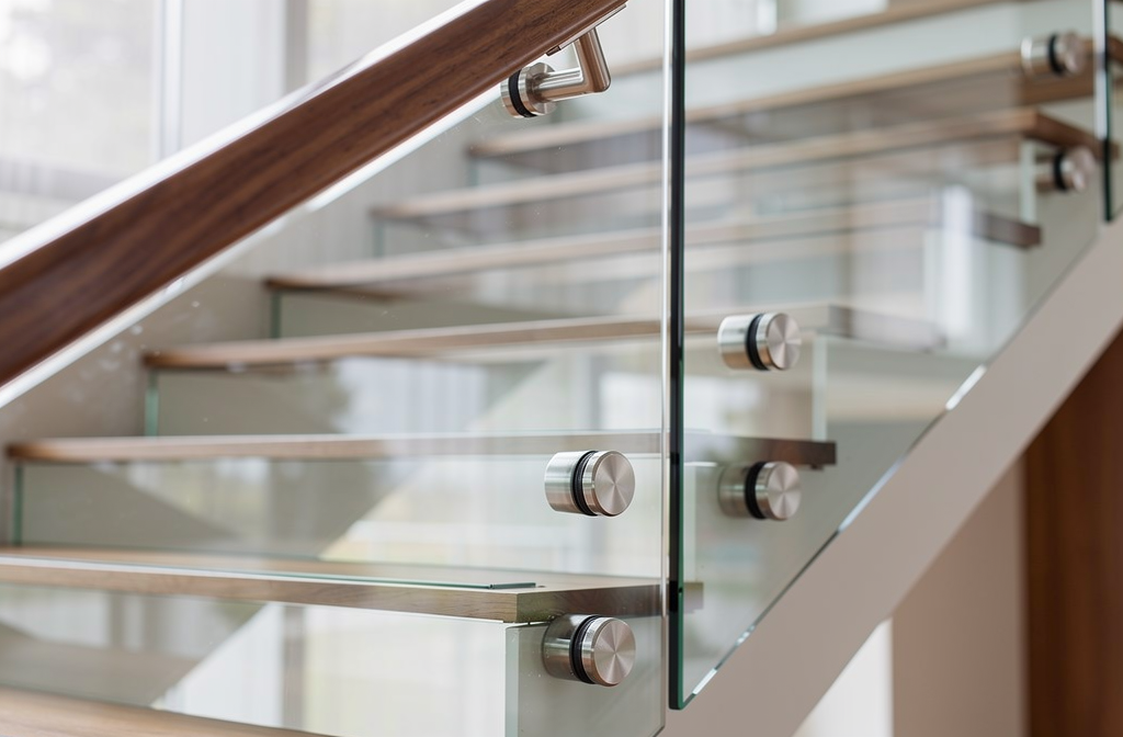 Pince à verre en acier inoxydable fixant un panneau de verre sur un garde-corps d'escalier moderne.