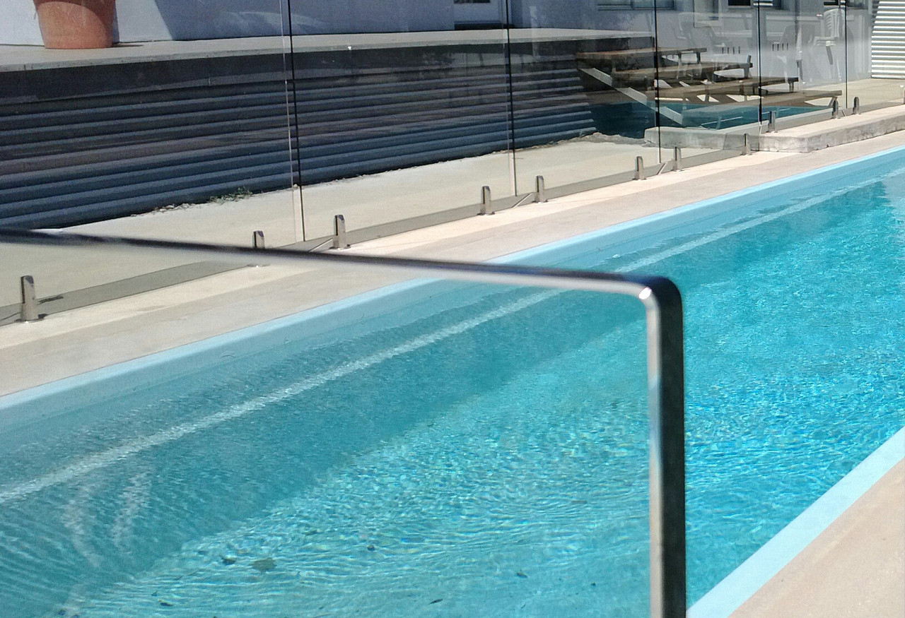 Garde-corps en verre Transparent autour d’une piscine extérieure, avec rail métallique et murs en façade vitrée.