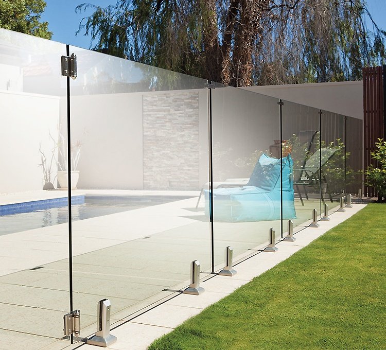 Garde-corps en verre transparent autour d'une piscine extérieure, montants et fixations en métal, cadre moderne et espace de lawn adjacent.