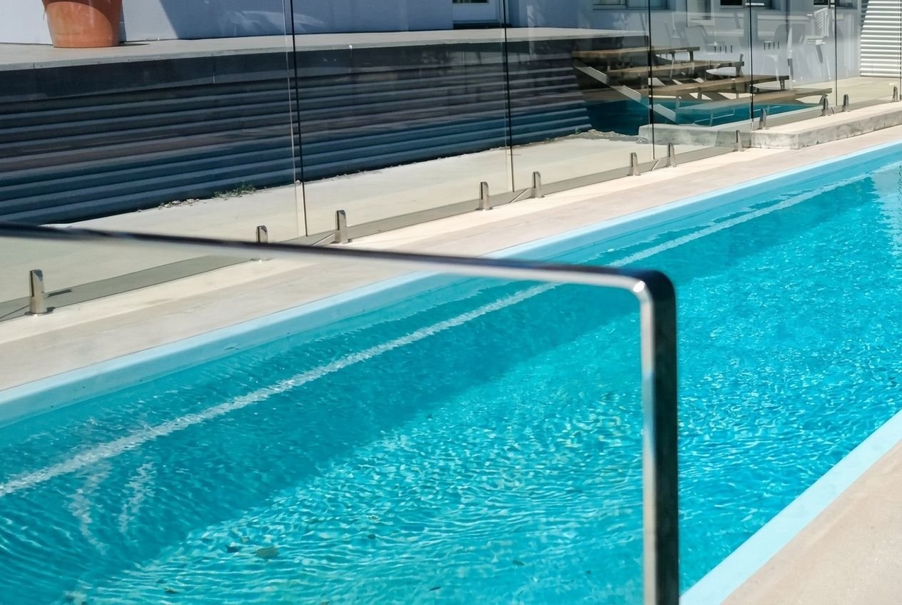 Garde-corps en verre sans cadre installé autour d'une piscine extérieure sur une terrasse moderne.